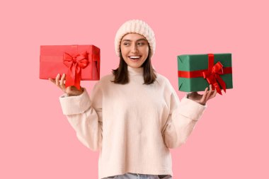 Pembe arka planda Noel hediyeleri olan genç bir kadın.