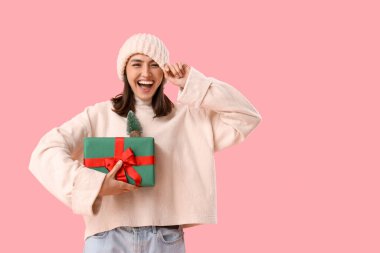 Pembe arka planda Noel hediyesi olan genç bir kadın.