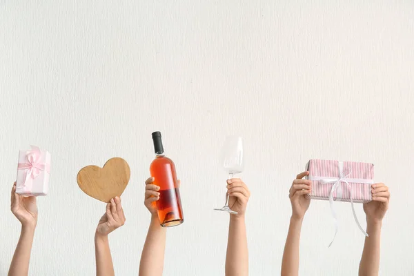 Female hands with bottle of wine, glass, gift box and wooden heart on light background