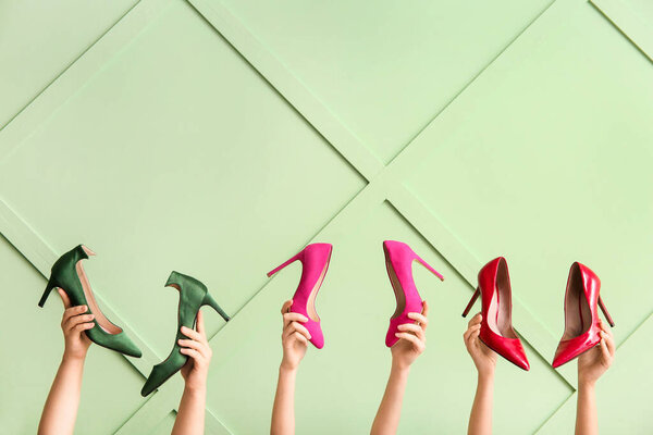 Female hands with stylish high heeled shoes against color wall