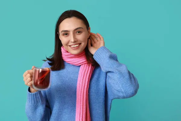 Happy young woman in scarf with glass cup of hot mulled wine on blue background