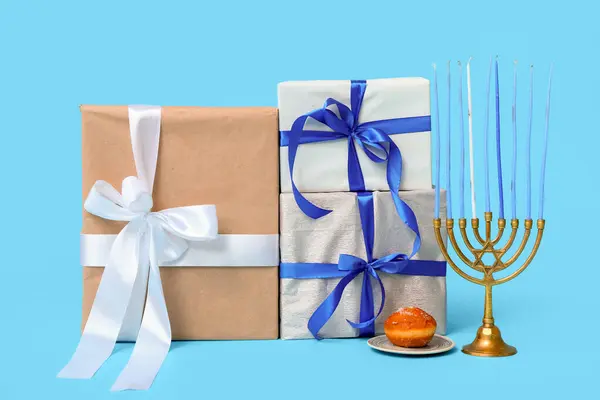 Gifts for Hanukkah celebration, menorah and donut on color background