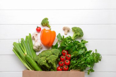 Taze sebzeler, mantarlar ve beyaz ahşap arka planda yeşillik içeren kağıt torba.