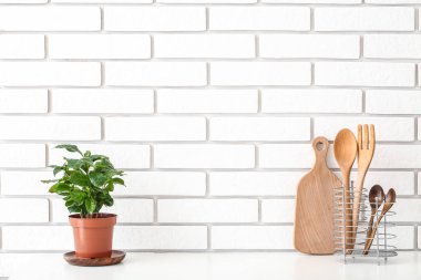 Mutfak gereçleri ve ev bitkileri beyaz tuğla duvarın yanındaki masada.