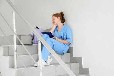 Bayan tıp öğrencisi üniversitenin merdivenlerinde okuyor.