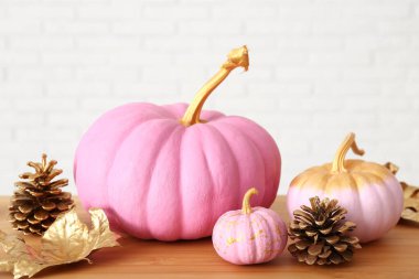 Sonbahar yapraklı pembe balkabakları ve beyaz tuğla duvarın yanındaki ahşap masada koniler.