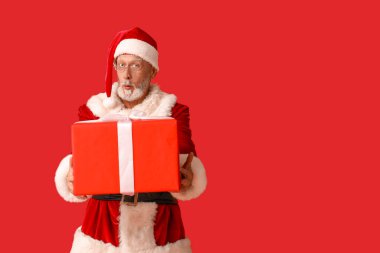 Kırmızı arka planda hediye kutusuyla Noel Baba 'yı şok etti.