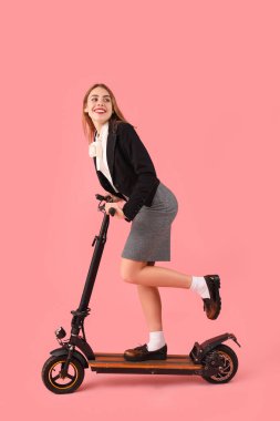 Pembe arka planda scooter süren genç bir iş kadını portresi.