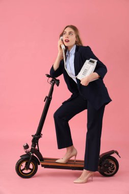 Tekme scooterlı genç bir iş kadınının portresi pembe arka planda telefonla konuşuyor.