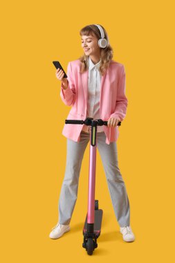Akıllı telefon, kulaklık ve scooter 'la sarı arka planda müzik dinleyen genç bir kadının portresi.