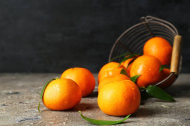 Tatlı mandalinalı sepet ve gri masada yapraklar.