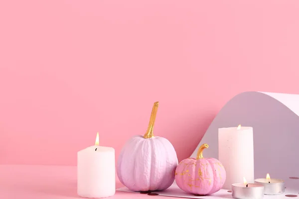 Different painted pumpkins and burning candles on colorful background