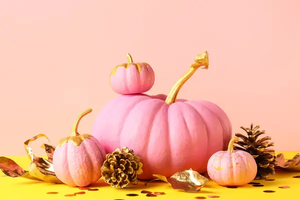 Pink painted pumpkins with golden leaves and cones on colorful background