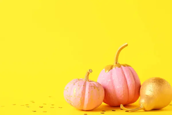 Pink painted pumpkins with golden pear and confetti on yellow background