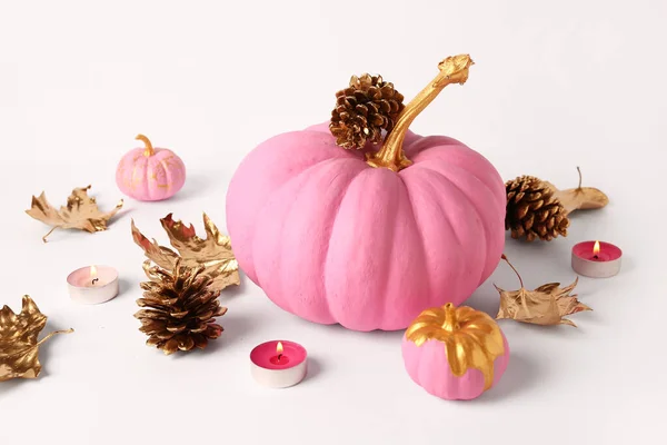 Pink painted pumpkins with golden cones and burning candles on white background