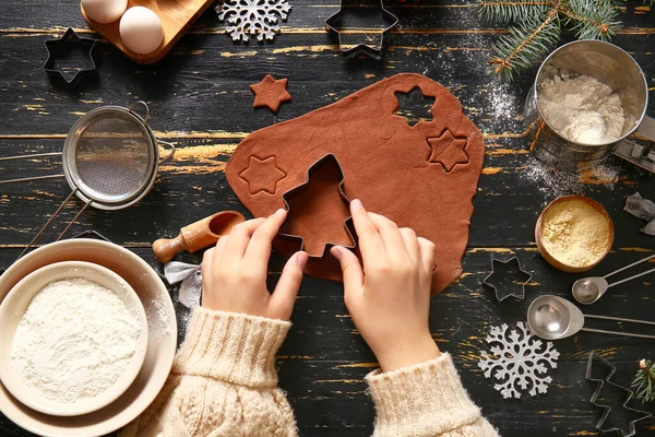 Siyah ahşap arka planda lezzetli Noel kurabiyeleri hazırlayan kadın.