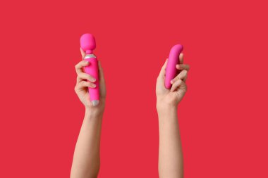Kırmızı arka planda vibratörleri olan kadın eller, yakın plan.