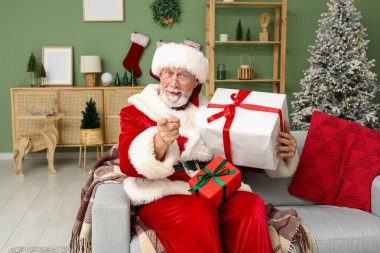 Noel Baba hediye kutularıyla Noel 'i evde koltukta kutluyor.