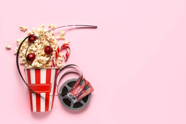 Bir kova patlamış mısır, film makarası, sinema biletleri ve pembe arka planda Noel dekoru.