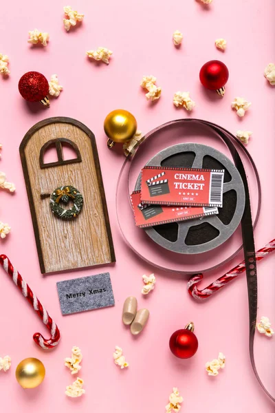 Film reel with cinema tickets, popcorn and Christmas decor on pink background