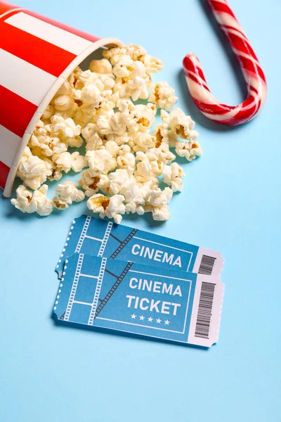 Bucket of popcorn with cinema tickets and candy cane on blue background