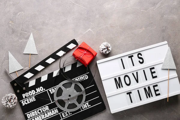 Movie clapper with text ITS MOVIE TIME,  film reel and Christmas decor on grey grunge background