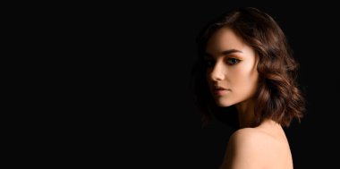 Siyah arka planda kıvırcık saçlı, metin için yeri olan güzel bir genç kadın.