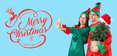 Elf kostümlü mutlu bir çift. Köknar ağacı ve cep telefonu mavi arka planda selfie çekiyor. Mutlu Noeller ve mutlu yıllar.