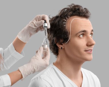 Genç adam gri arka planda saç büyümesi için serum tedavisi görüyor. 