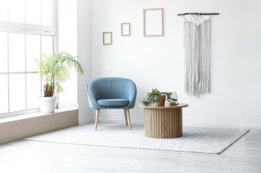 Işıl ışıl oturma odasının içi, rahat gri koltuğu ve ahşap sehpanın üzerindeki bitki örtüsü.