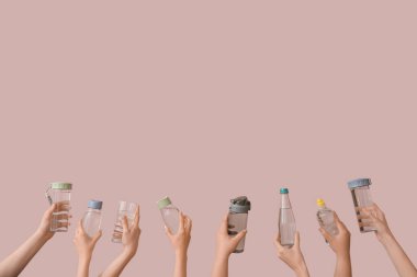 Şişeli kadın elleri ve pembe arka planda bir bardak soğuk su.