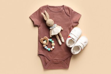 Pamuk bebek kıyafetleri, örgü oyuncaklar ve turuncu arka planda çıngırak.