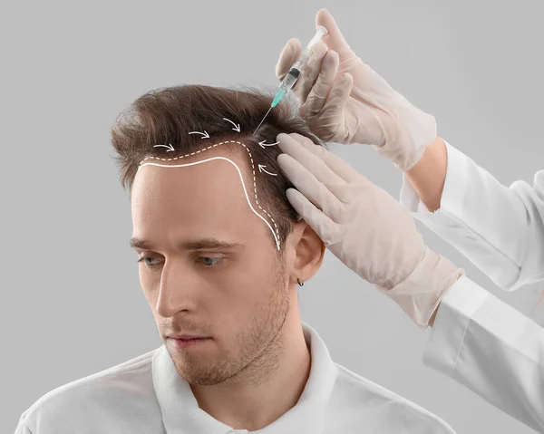 Young man receiving injection for hair growth on grey background