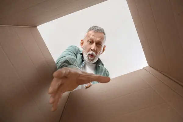 Surprised mature man with open parcel at home, view from inside