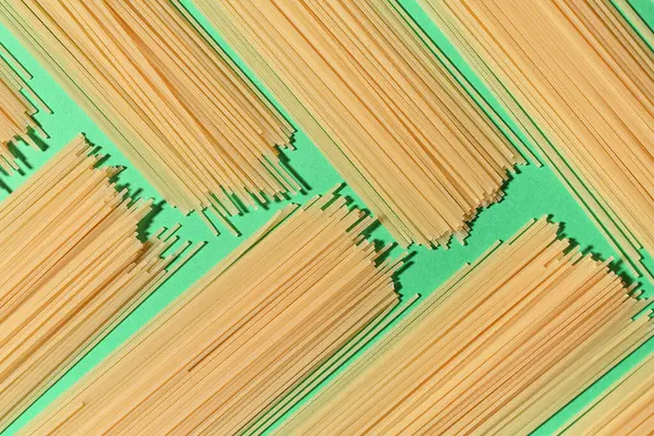 Composition with uncooked spaghetti pasta on green background