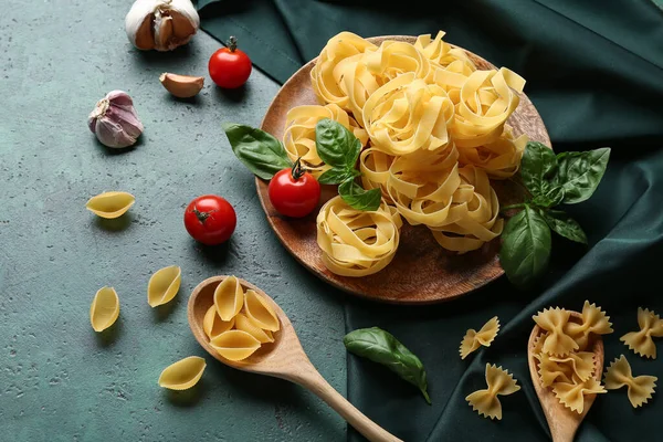 Composition with different uncooked pasta, spices and tomatoes on green background, closeup