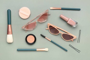 Yeşil zemin üzerinde şık güneş gözlüğü ve makyaj ürünleri olan kompozisyon