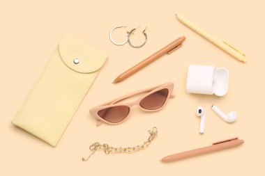 Şık güneş gözlüklü kompozisyon, modern kulaklıklar ve bej arka planda kadın aksesuarları.