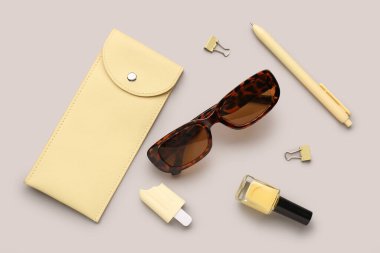 Şık güneş gözlüklü kompozisyon, gri arka planda oje ve kırtasiye malzemesi.