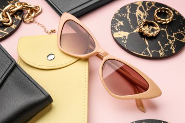 Pembe arka planda şık güneş gözlükleri, çanta ve kadın aksesuarları olan kompozisyon, yakın plan.