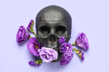 Siyah insan kafatası, mor arka planda güzel çiçekler.
