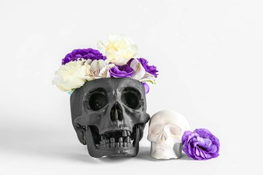Beyaz arka planda güzel çiçekler olan siyah insan kafatası.