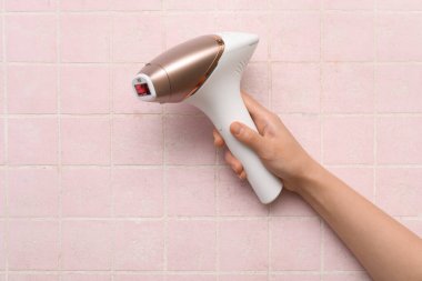 Pembe karo arka planında modern fotoepilatör olan kadın eli.