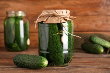 Konserve salatalıklı kavanoz ve ahşap arka planda taze sebze.