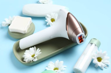 Kozmetik ürünleri, banyo malzemeleri ve mavi arka planda güzel çiçeklerle modern fotoepilatör.