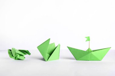 Beyaz arka planda bayraklı, çiçekli ve buruşuk kağıtlı yeşil origami teknesi