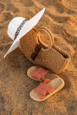 Havalı plaj çantası, parmak arası terlik, güneş gözlüğü ve kumda şapka.