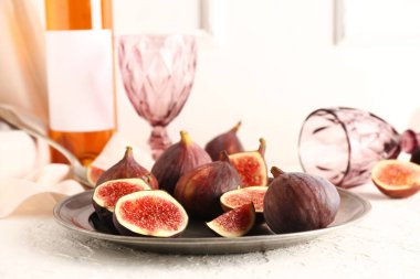 Taze incirli tabak ve beyaz arka planda bir şişe şarap.