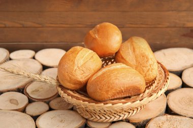 Tahta arka planda taze ekmek somunları ve buğday dikenleriyle dolu bir sepet.