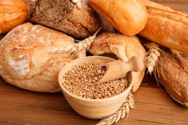 Farklı taze ekmek somunları ile buğday dikenleri ve tahıllar ahşap zemin üzerinde